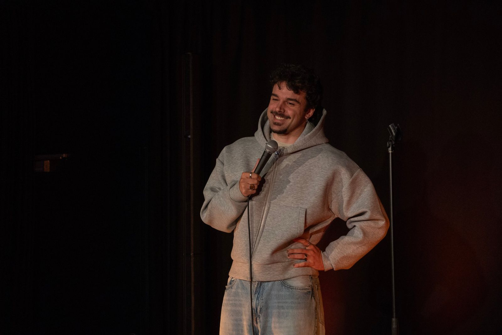 Sylvain Gautier, en sweat gris, micro en main et main sur la hanche, sourit au public sur la scène de L'Estrade