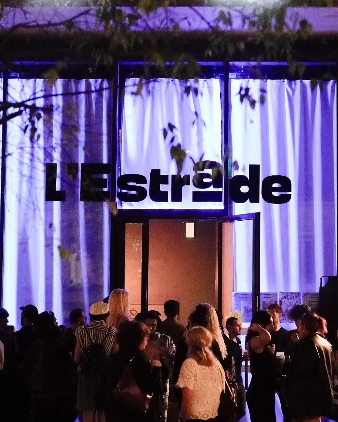 La façade de L'Estrade éclairée le soir, le public rassemblé devant l'entrée